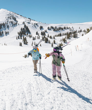 two women hiking carrying skis on shoulders