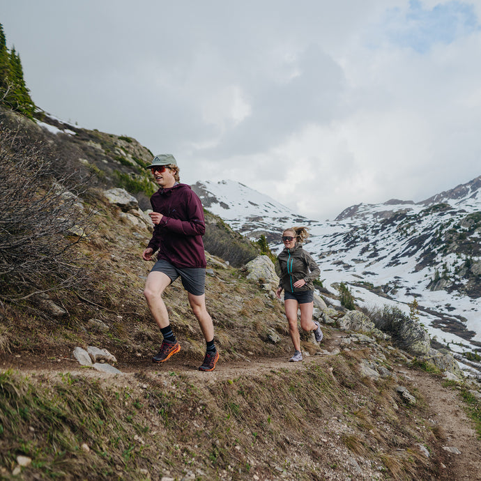 man and woman running thawed out high alpine mountain trail wearing scout jackets