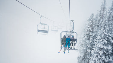 3 friends riding chairlift through snowy trees